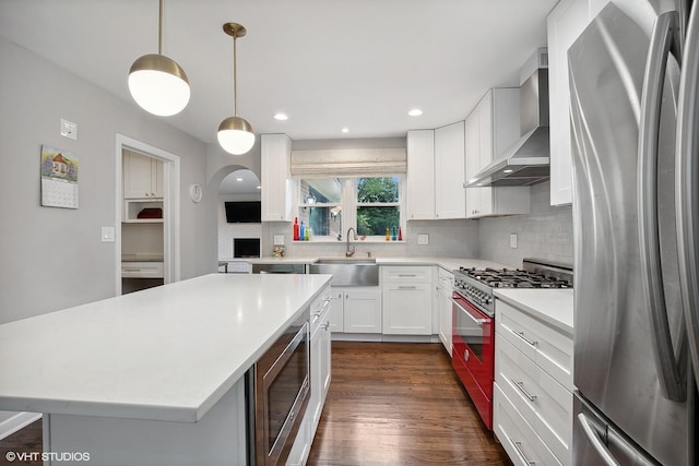 kitchen with sink, a center island, wall chimney range hood, pendant lighting, and appliances with stainless steel finishes