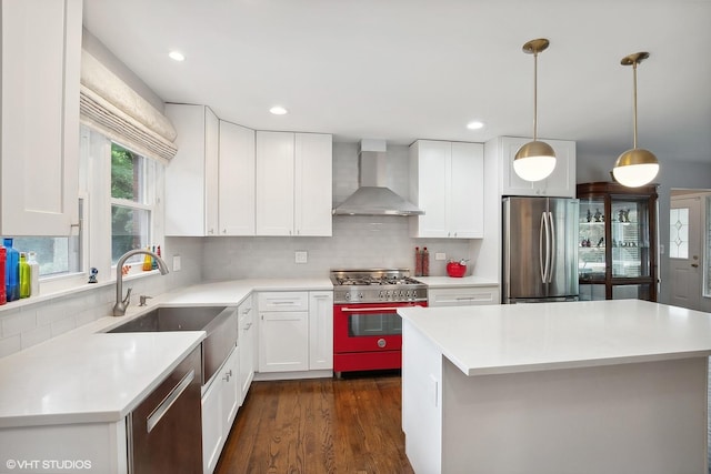 kitchen featuring appliances with stainless steel finishes, sink, wall chimney range hood, pendant lighting, and white cabinetry