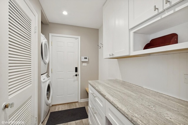 washroom with cabinets, stacked washing maching and dryer, and light hardwood / wood-style flooring