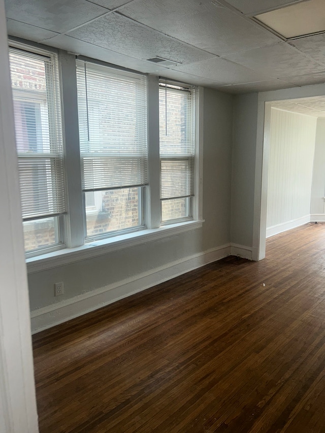 empty room with plenty of natural light, dark wood-type flooring, and a drop ceiling