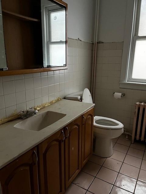 bathroom featuring vanity, radiator, tile patterned flooring, toilet, and tile walls