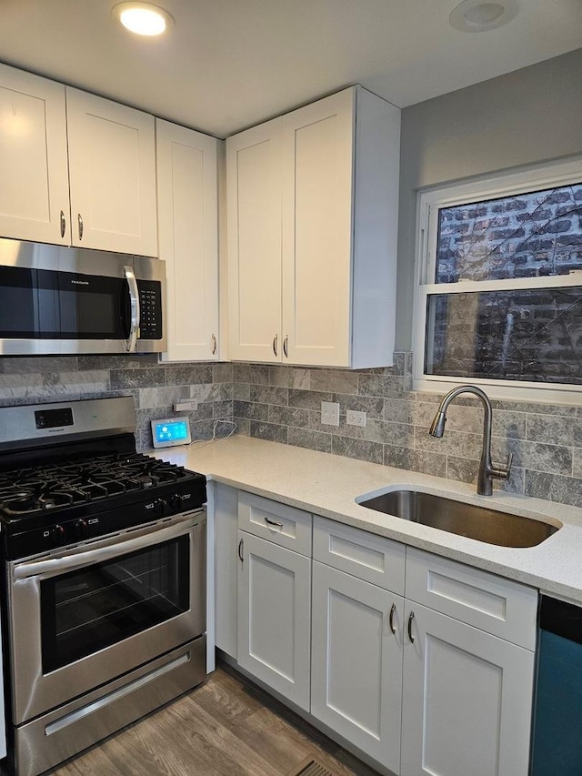 kitchen featuring appliances with stainless steel finishes, tasteful backsplash, sink, hardwood / wood-style flooring, and white cabinetry