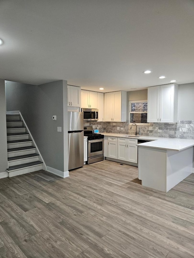 kitchen with white cabinets, appliances with stainless steel finishes, light hardwood / wood-style floors, and decorative backsplash