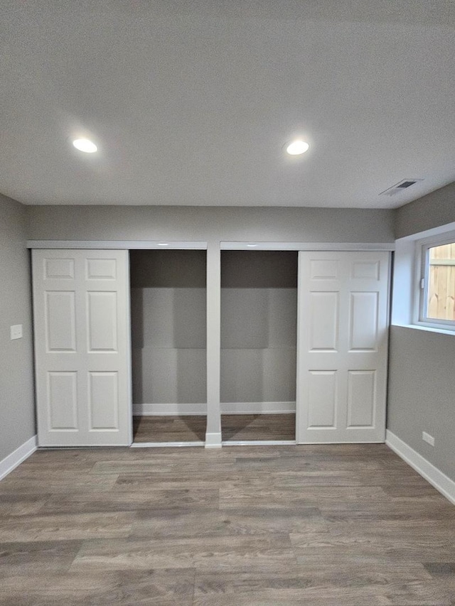 unfurnished bedroom featuring wood-type flooring, a textured ceiling, and multiple closets