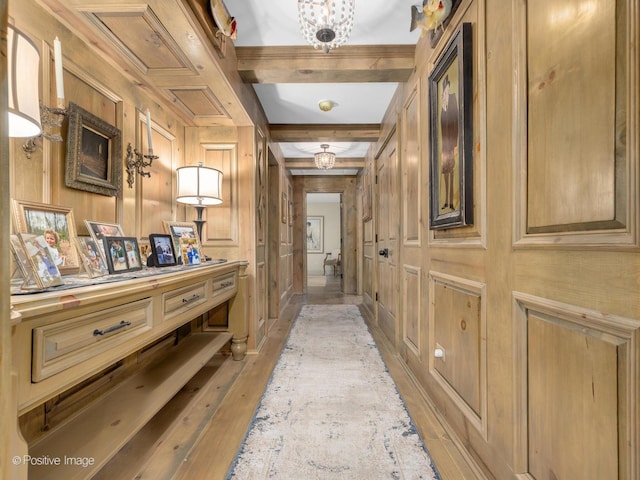 hall with wooden walls, hardwood / wood-style floors, beamed ceiling, and a chandelier