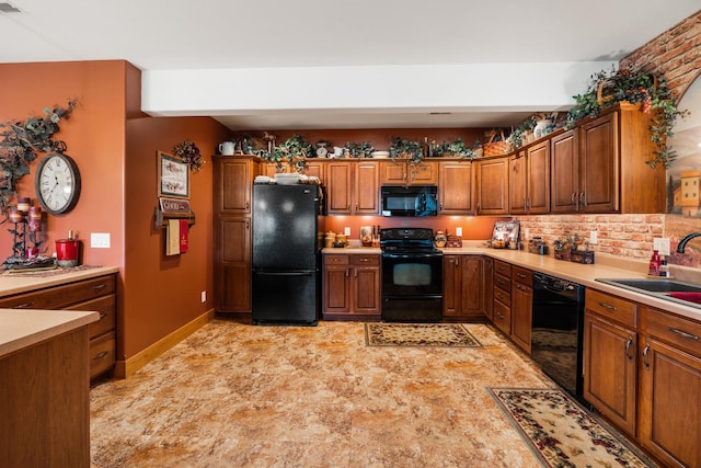 kitchen featuring a sink, baseboards, light countertops, black appliances, and brown cabinetry