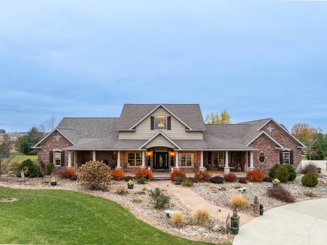 view of front of property featuring a porch, brick siding, a shingled roof, and a front lawn