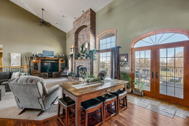 living room with a fireplace, high vaulted ceiling, a ceiling fan, and french doors