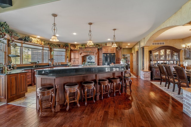 kitchen featuring a kitchen island, arched walkways, black refrigerator with ice dispenser, and a kitchen breakfast bar