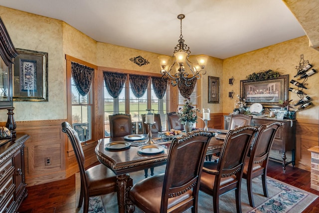 dining area with dark wood-type flooring, a wainscoted wall, and a notable chandelier