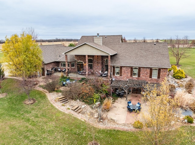 back of house featuring a shingled roof, a lawn, a patio, a chimney, and brick siding