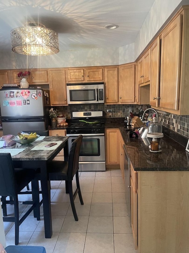 kitchen featuring stainless steel appliances, a notable chandelier, dark stone counters, pendant lighting, and light tile patterned floors