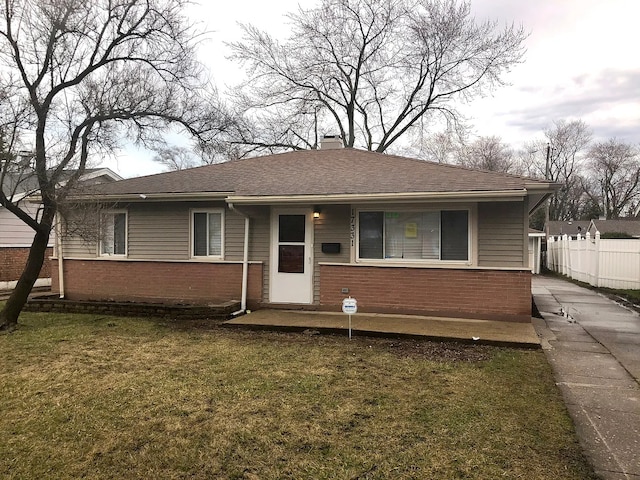 view of front of property featuring a shingled roof, a chimney, fence, a front lawn, and brick siding