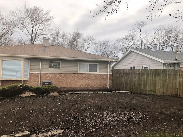 view of home's exterior with brick siding, fence, a chimney, and roof with shingles