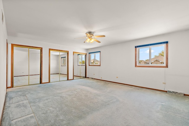 unfurnished bedroom featuring multiple closets, ceiling fan, and light colored carpet