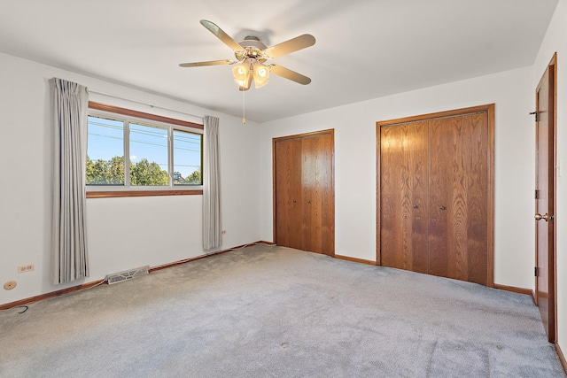 unfurnished bedroom with ceiling fan, light colored carpet, and multiple closets