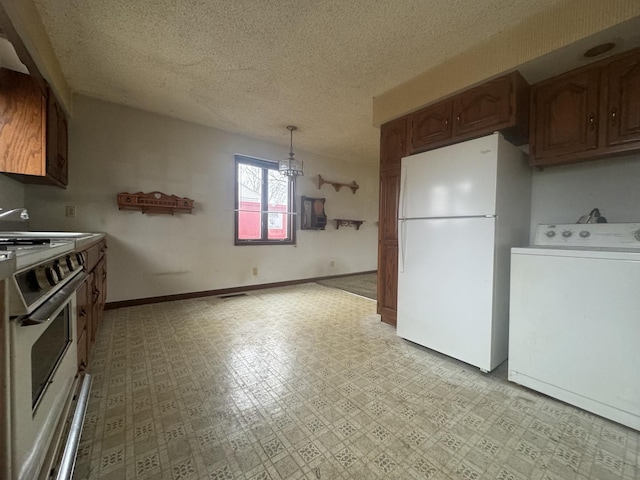 kitchen featuring sink, white refrigerator, stove, pendant lighting, and washer / dryer