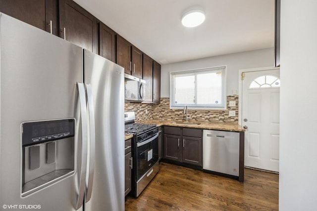 kitchen featuring light stone counters, dark brown cabinets, stainless steel appliances, dark wood-type flooring, and sink