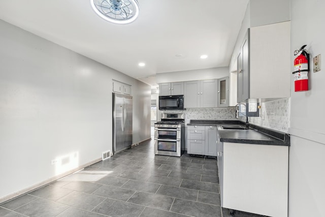 kitchen featuring gray cabinetry, backsplash, dark tile patterned flooring, sink, and appliances with stainless steel finishes