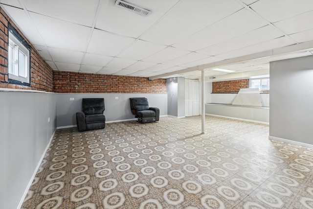 basement featuring a paneled ceiling and brick wall