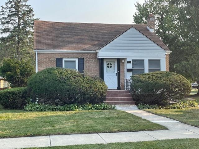 view of front of property with roof with shingles, brick siding, a front lawn, and a chimney