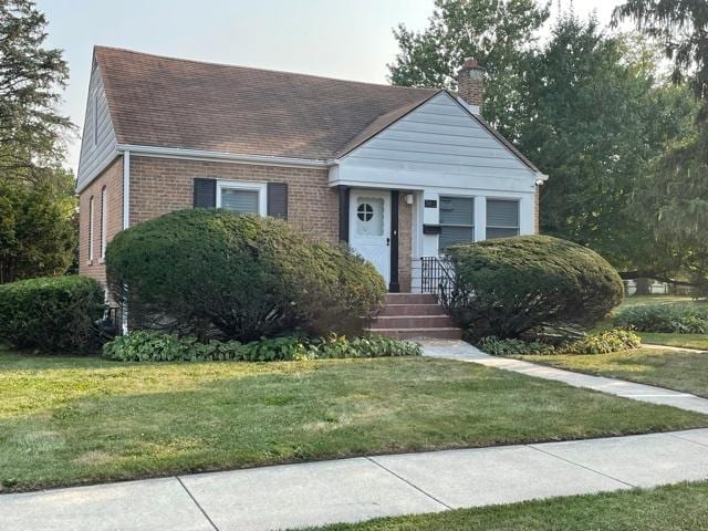 bungalow-style house with a chimney, brick siding, roof with shingles, and a front yard