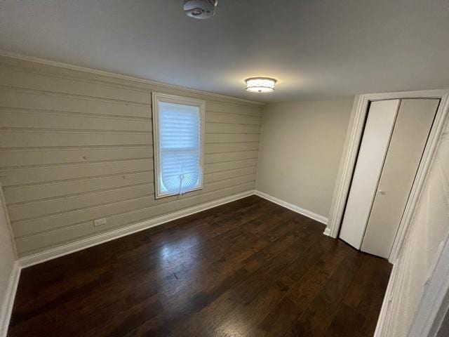 unfurnished bedroom featuring wooden walls, a closet, baseboards, and dark wood-style flooring