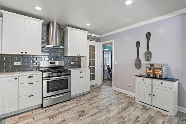 kitchen with stainless steel range with gas cooktop, ornamental molding, wall chimney range hood, decorative backsplash, and white cabinets