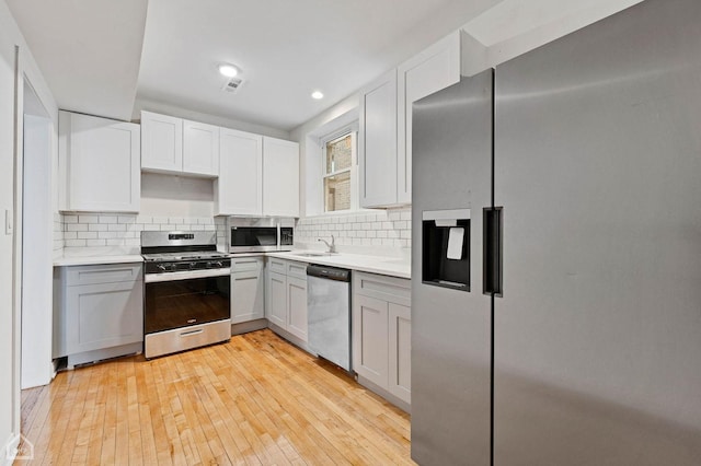 kitchen with backsplash, white cabinetry, light wood-type flooring, and stainless steel appliances