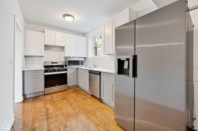 kitchen with gray cabinets, light hardwood / wood-style floors, stainless steel appliances, and tasteful backsplash