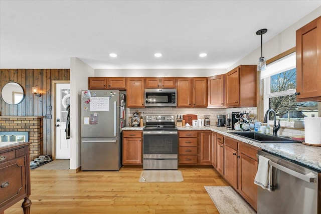 kitchen with stainless steel appliances, sink, light stone counters, and decorative light fixtures