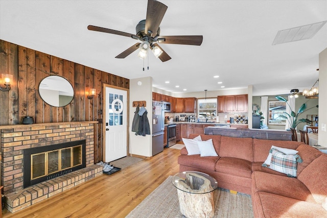 living room featuring a fireplace, ceiling fan, and light wood-type flooring