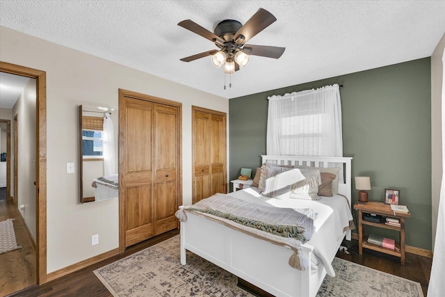 bedroom with multiple closets, dark wood-type flooring, a textured ceiling, and ceiling fan