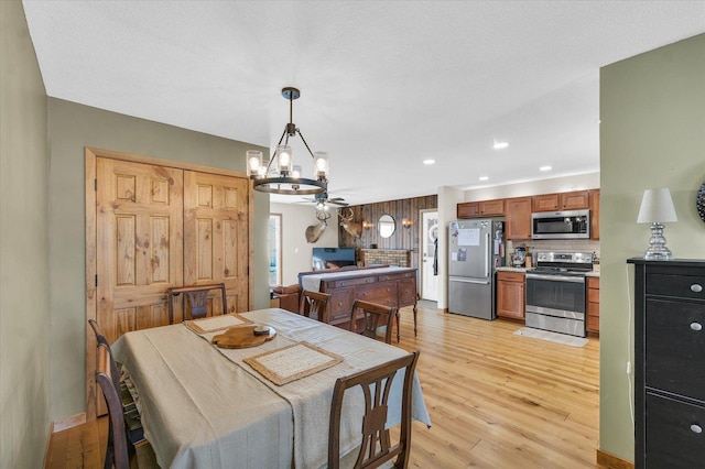 dining space featuring ceiling fan with notable chandelier and light hardwood / wood-style floors