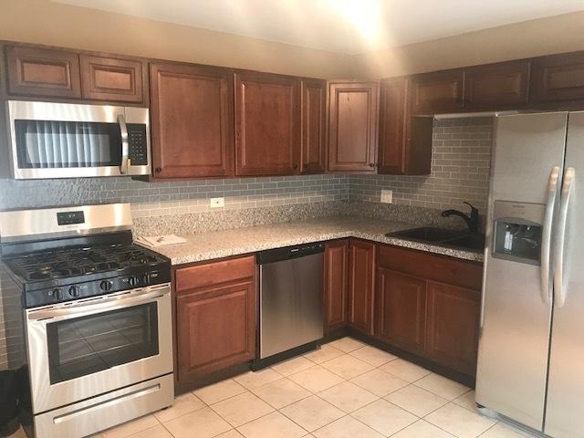 kitchen with stainless steel appliances, light stone counters, backsplash, and a sink