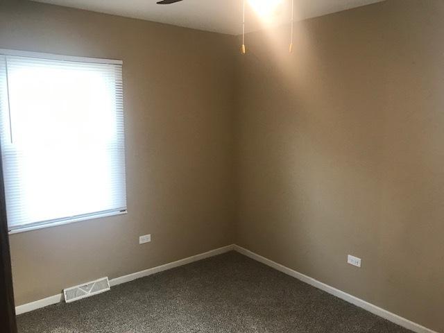 empty room featuring dark colored carpet, visible vents, ceiling fan, and baseboards