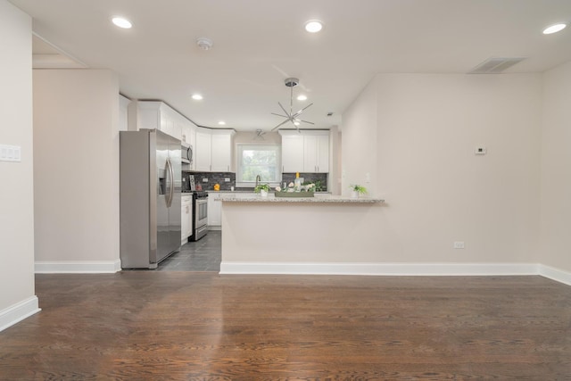 kitchen with white cabinets, appliances with stainless steel finishes, a peninsula, light stone countertops, and backsplash