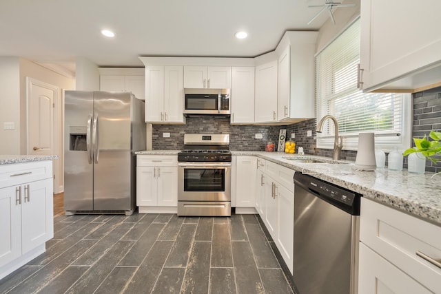 kitchen with appliances with stainless steel finishes, white cabinetry, a sink, and light stone countertops