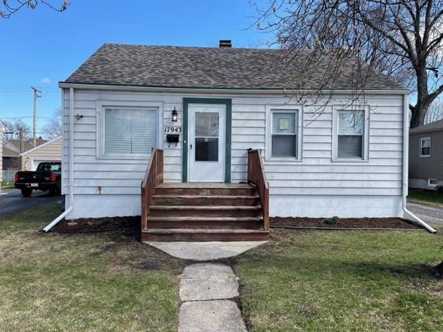 bungalow featuring entry steps, roof with shingles, a chimney, and a front lawn