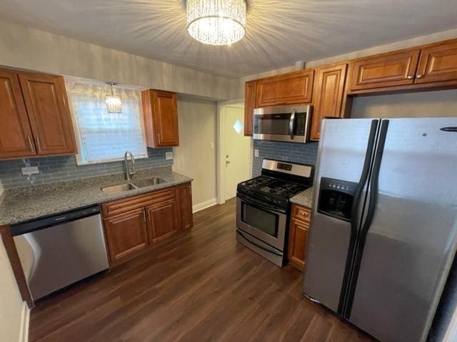 kitchen featuring brown cabinetry, light stone counters, appliances with stainless steel finishes, dark wood-type flooring, and a sink