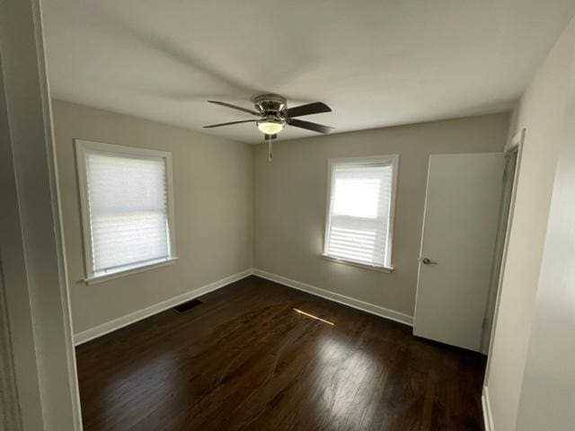 spare room with a ceiling fan, visible vents, dark wood finished floors, and baseboards