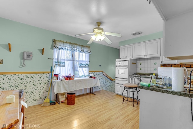 kitchen featuring backsplash, ceiling fan, light hardwood / wood-style flooring, white cabinets, and oven