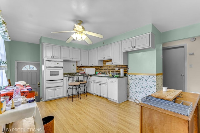 kitchen featuring backsplash, ceiling fan, light hardwood / wood-style flooring, white cabinets, and oven