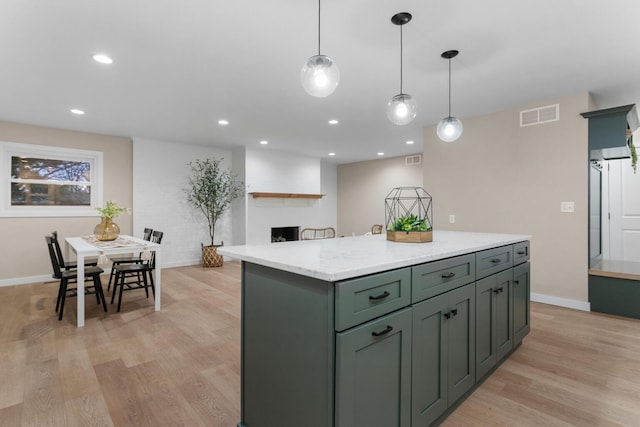 kitchen with light stone counters, a large fireplace, decorative light fixtures, light hardwood / wood-style flooring, and a kitchen island