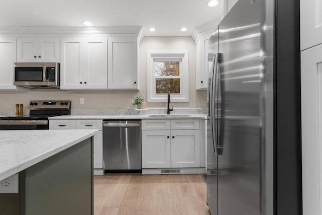 kitchen featuring sink, light hardwood / wood-style flooring, light stone countertops, appliances with stainless steel finishes, and white cabinetry