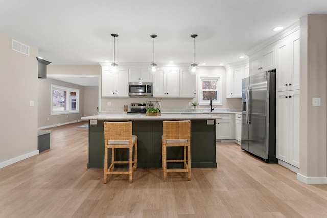 kitchen with white cabinetry, decorative light fixtures, a breakfast bar area, a kitchen island, and appliances with stainless steel finishes