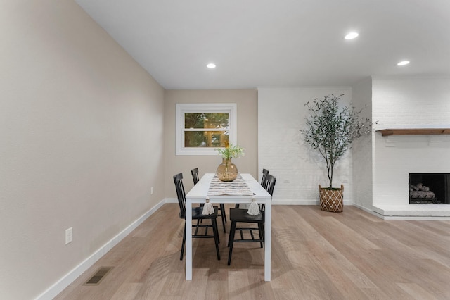 dining area with light hardwood / wood-style flooring, brick wall, and a brick fireplace