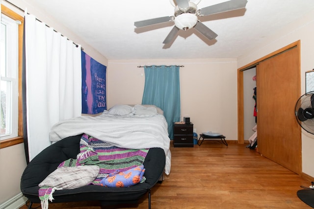 bedroom with hardwood / wood-style flooring, ceiling fan, baseboard heating, and a closet