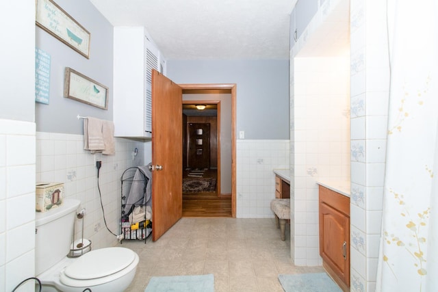 bathroom featuring tile patterned floors, a textured ceiling, toilet, vanity, and tile walls