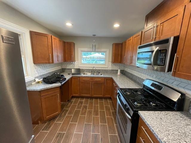 kitchen featuring brown cabinets, stainless steel appliances, a sink, and decorative light fixtures